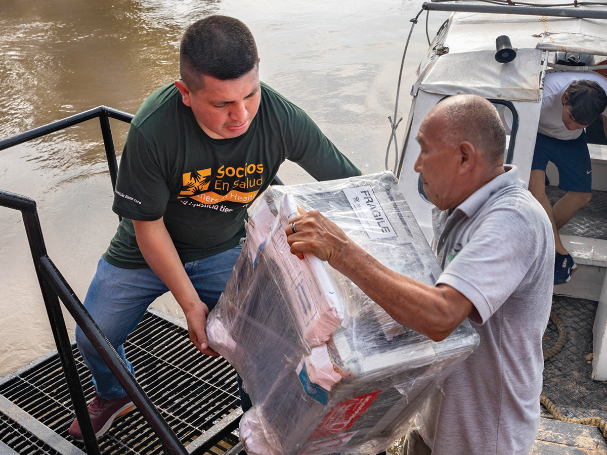 A person in a green Socios en Salud shirt helps another person unload a fragile parcel
