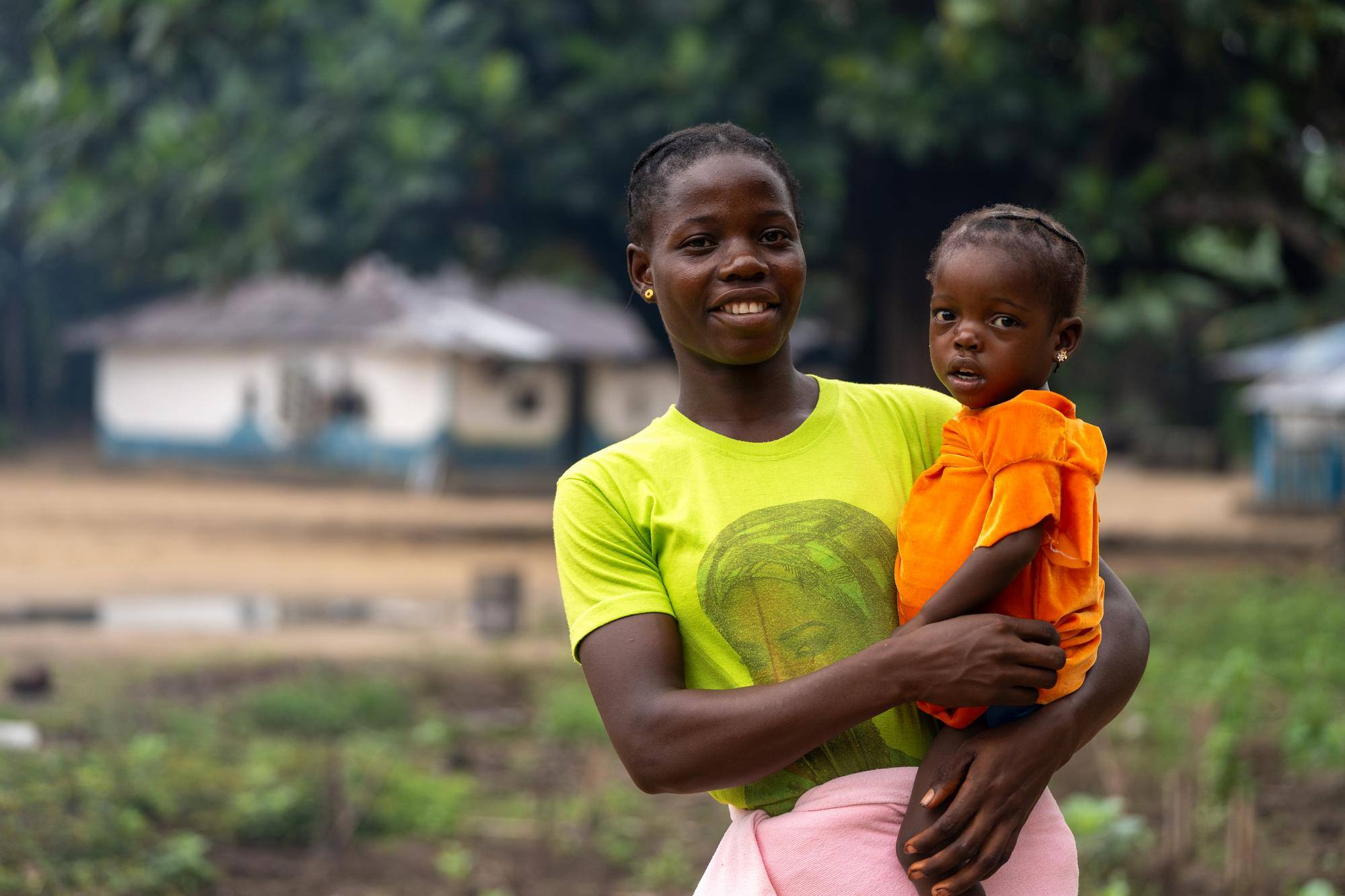 A person in a bright yellow shirt smiles and holds a small child wearing a bright orange shirt