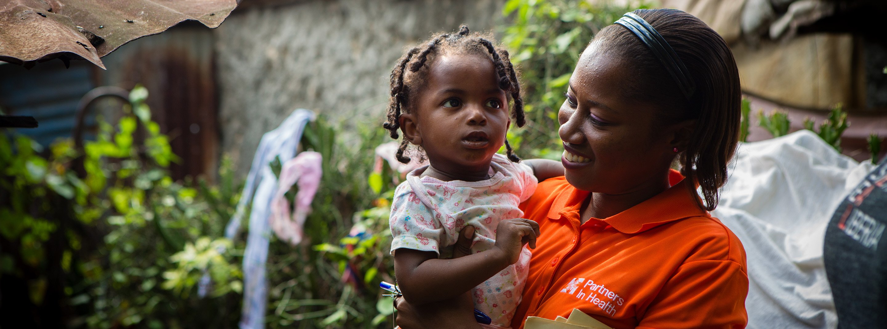 A PIH worker cheerily carries a toddler during a home visit.